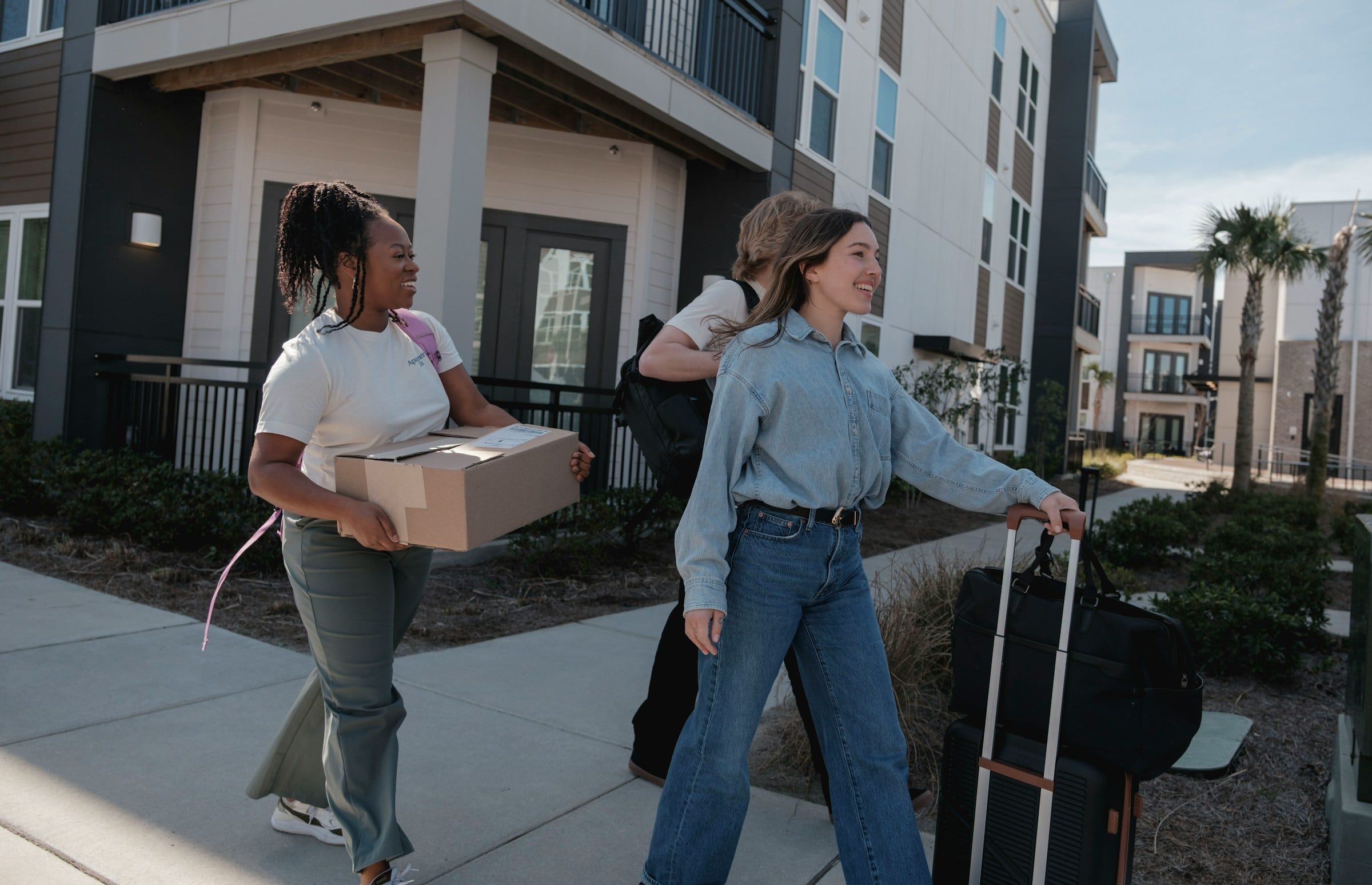 Carrying moving boxes and luggage outside a palm-lined apartment building