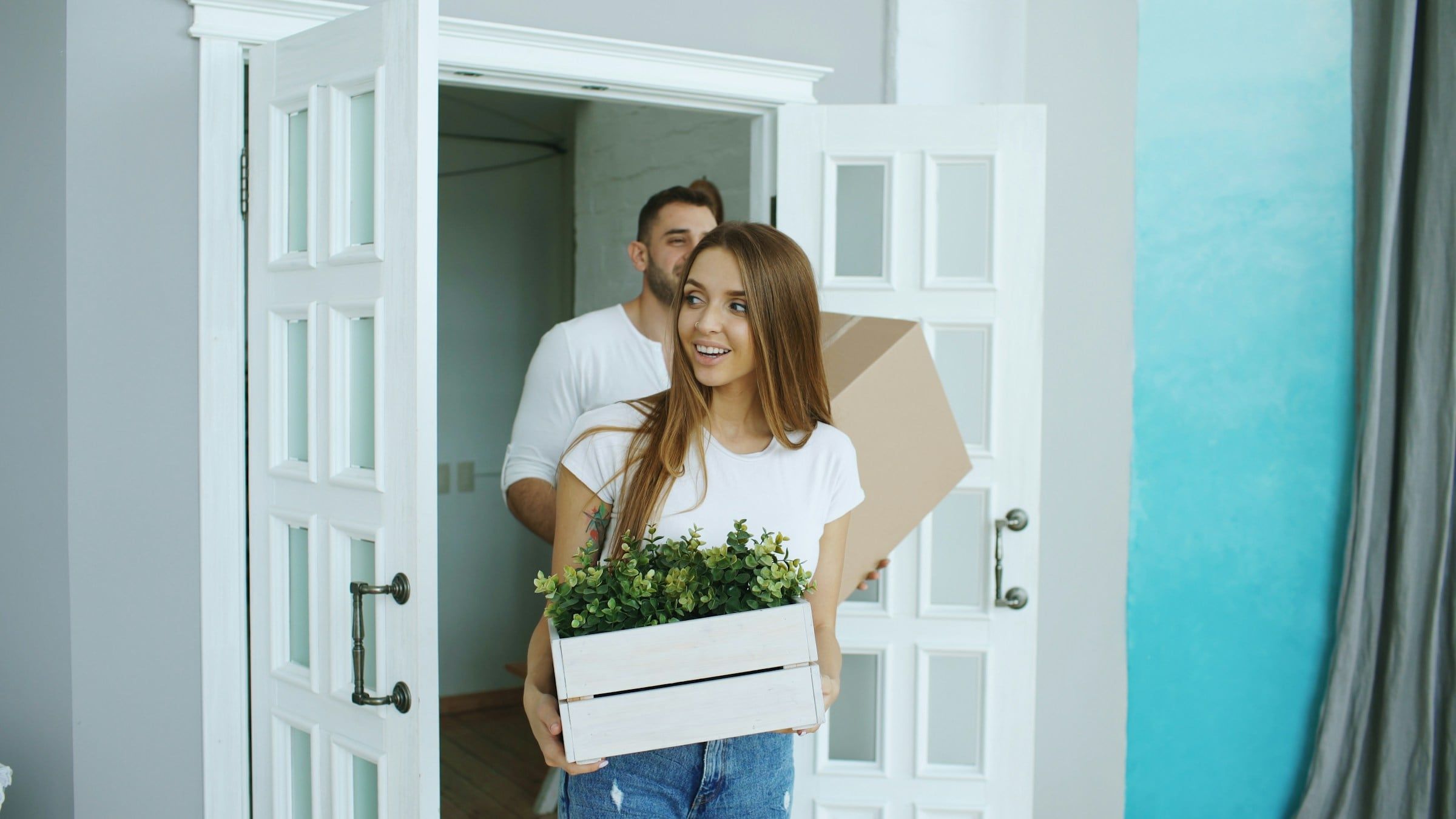 Carrying a moving box and plants through the front door of a new home